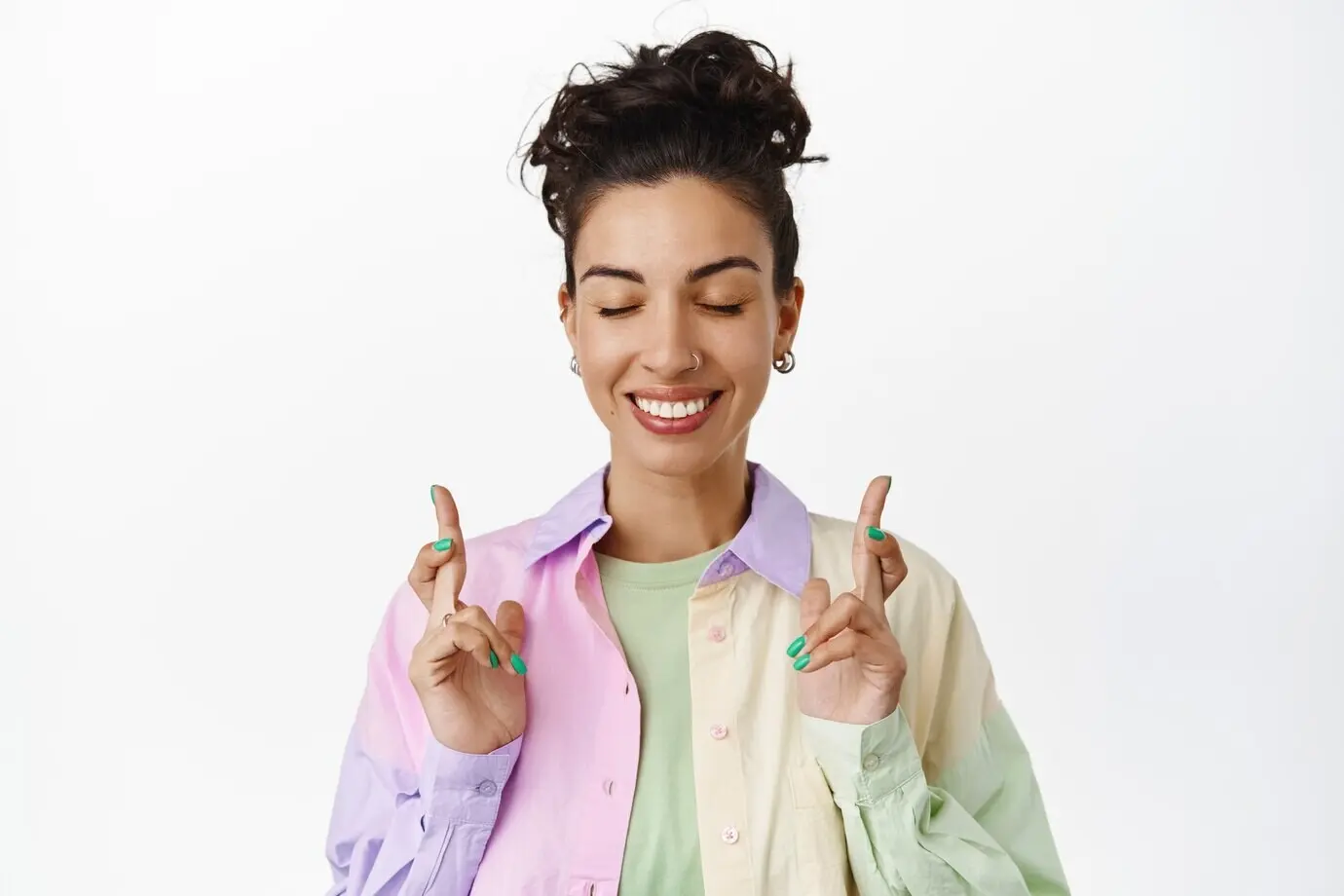 Hoffnungsvoll lächelndes brünettes Mädchen, das sich etwas wünscht, die Finger kreuzt und die Augen schließt, in Erwartung der Ergebnisse, wartend darauf, dass ein Traum wahr wird, betend, auf Weiß stehend.